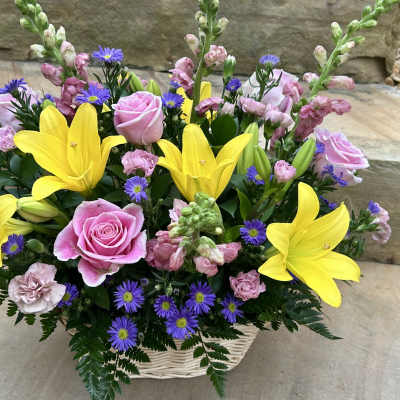 Basket arrangement with pink roses, yellow lilies, and purple daisies