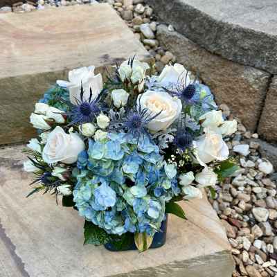 Blue hydrangeas and white roses arranged in a low square vase