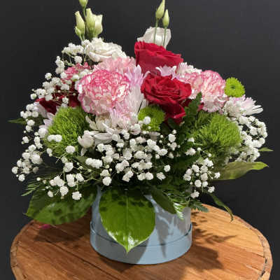 Mixed bouquet of red and pink roses with white filler flowers in a round box