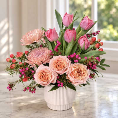 Pink tulips and peach flowers arranged in a white vase
