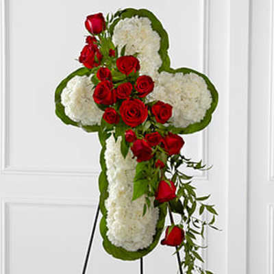 Cross-shaped floral tribute with red roses and white blooms on an easel