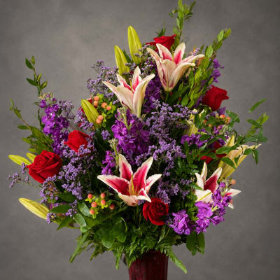 Tall bouquet of red roses and pink lilies in a red vase