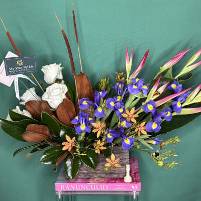 Arrangement of white roses, purple irises, and pink tropical blooms in a rectangular vase