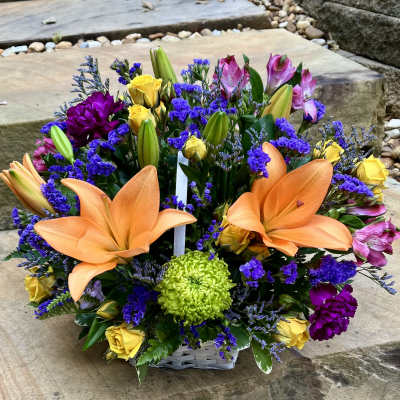 Mixed bouquet with orange lilies, yellow roses, and purple flowers in a basket