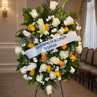 Standing floral wreath of white and yellow roses with a memorial ribbon