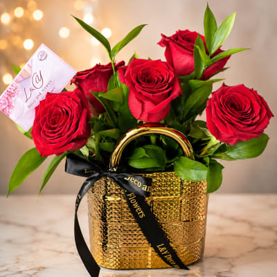 Red roses arranged in a gold basket with a black ribbon