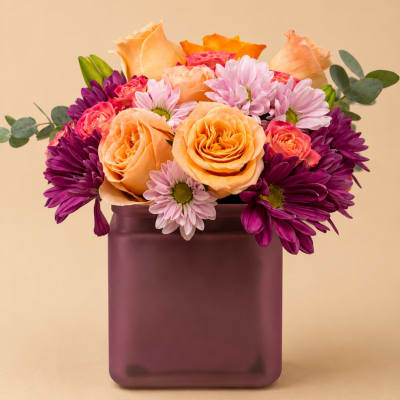 Peach roses and purple daisies in a square vase