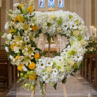 Heart-shaped floral wreath on an easel with white and yellow flowers