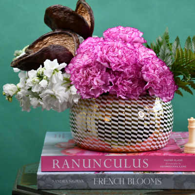 Pink carnations and white flowers in a patterned vase with greenery
