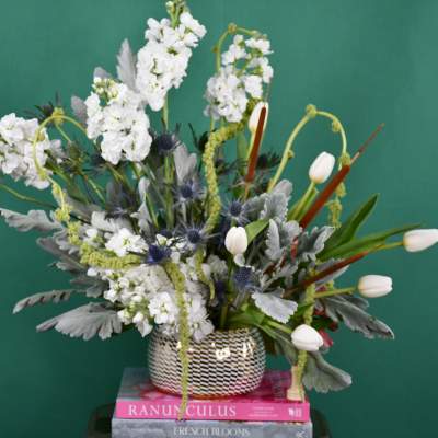 Tall white floral arrangement in a patterned vase with tulips and spiky blue accents