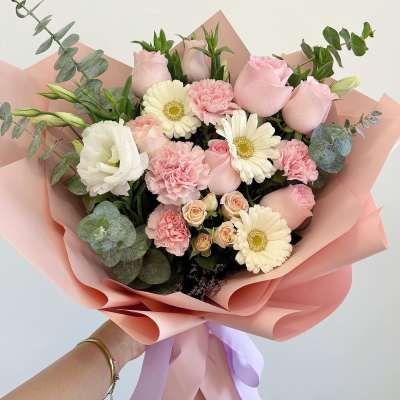 Handheld bouquet of pink roses, white gerbera daisies, and carnations wrapped in pink paper
