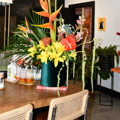 Tropical flower arrangement with yellow lilies and orange bird-of-paradise in a dark vase