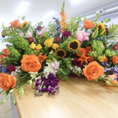 Large mixed floral arrangement with orange roses, sunflowers, and lilies on a table