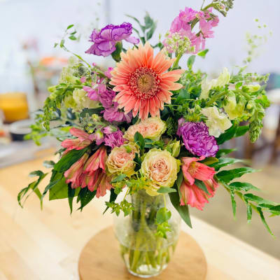 Mixed bouquet of pink, peach, and purple flowers in a clear glass vase