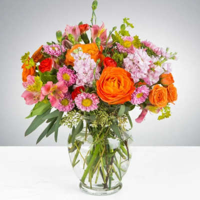 Mixed bouquet of orange, pink, and red flowers in a clear glass vase