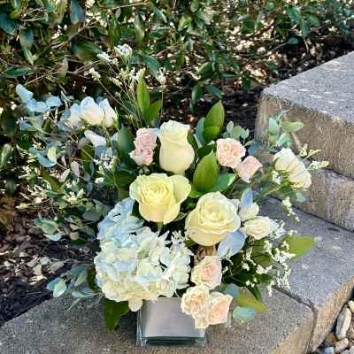 Arrangement of cream roses, pale hydrangea, and eucalyptus in a square glass vase