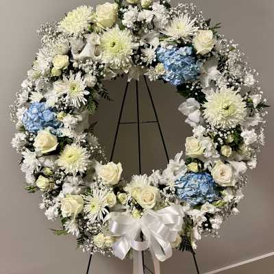 Large white floral wreath with blue hydrangeas on a black stand