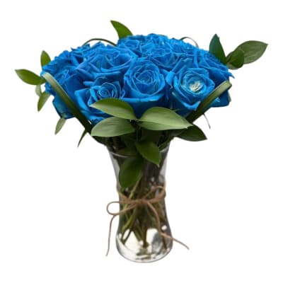Blue roses arranged in a clear glass vase with greenery
