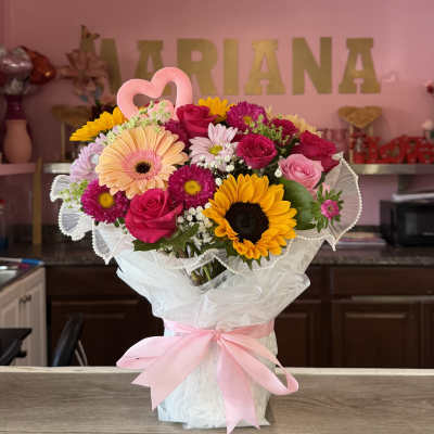 Bouquet of pink, yellow, and white flowers wrapped in white paper with a pink ribbon