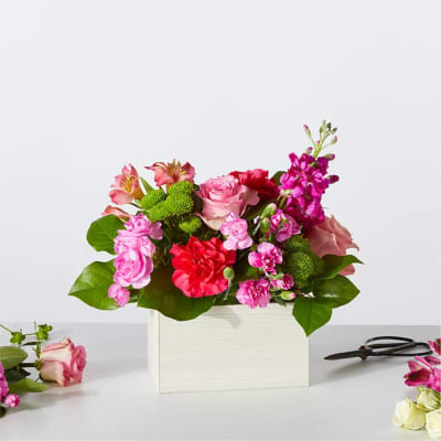 Pink and red flower arrangement in a white box with green foliage