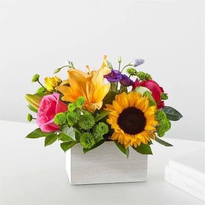Mixed bouquet with sunflowers, roses, lilies, and purple blooms in a white box