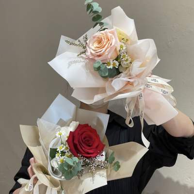 Two wrapped rose bouquets, one red and one blush pink, with small white daisies