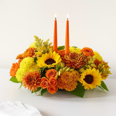 Orange and yellow floral centerpiece with two lit orange candles