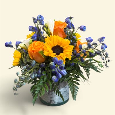 Bouquet of sunflowers, orange roses, and blue flowers in a metal container