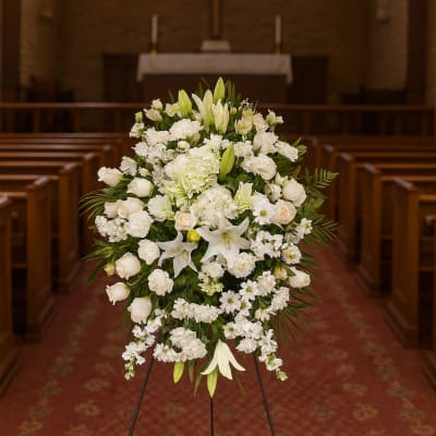 White funeral spray with lilies and roses on a stand in a church
