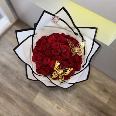 Bouquet of red roses wrapped in white paper with black trim and gold butterfly accents