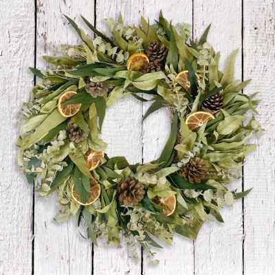 Green wreath with dried orange slices and pinecones on a white wood background