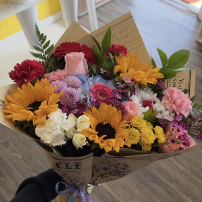 Handheld bouquet with sunflowers, roses, carnations, and mixed blooms in paper wrap