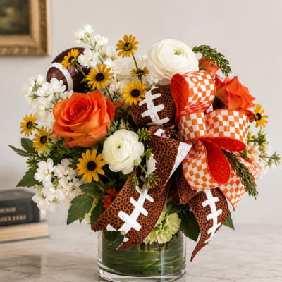 Bouquet of orange and white flowers in a glass vase with football ribbons