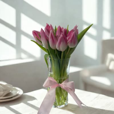 Pink tulips in a clear glass vase with a pink ribbon