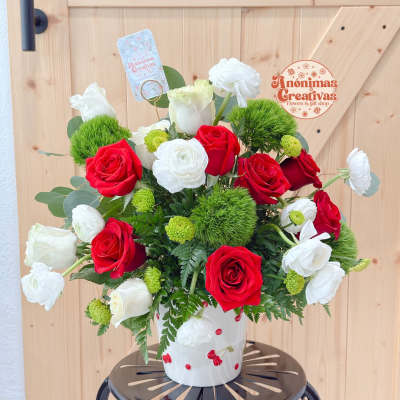 Red and white roses arranged in a white vase with green accents