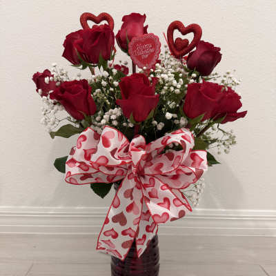 Red roses in a dark vase with a heart-patterned bow and Valentine topper