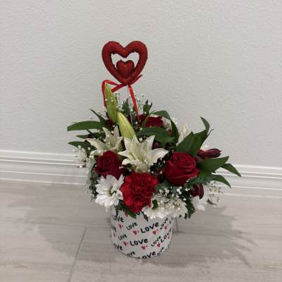 Red and white floral arrangement in a heart-decorated box with a heart topper