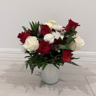 Red and white roses with white daisies in a clear glass vase