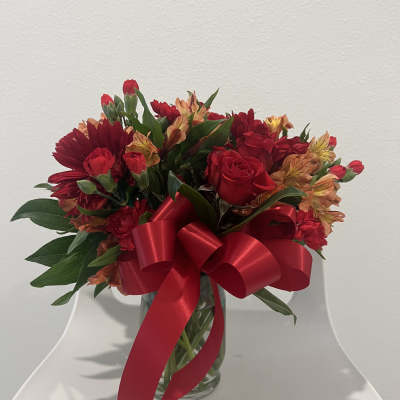 Red and orange mixed bouquet in a glass vase with a large red ribbon