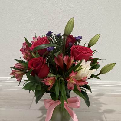Bouquet of red roses, lilies, and pink flowers in a glass vase with a pink ribbon