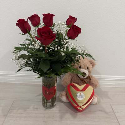 Red roses in a glass vase with a teddy bear and heart-shaped chocolate box