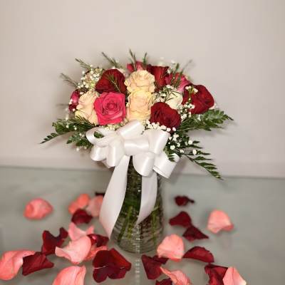 Bouquet of red, pink, and cream roses in a glass vase with a white ribbon