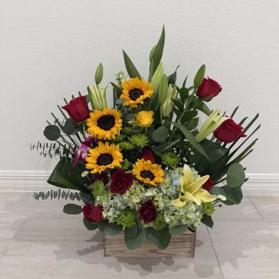Mixed bouquet with sunflowers, red roses, and lilies in a wooden box