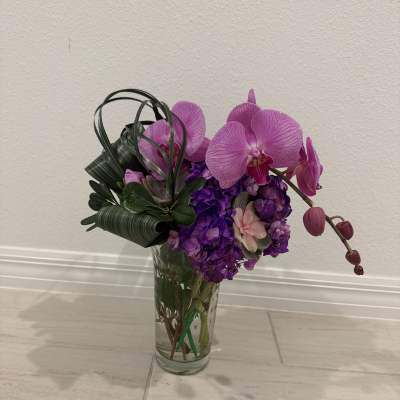 Purple orchids and hydrangeas arranged in a clear glass vase