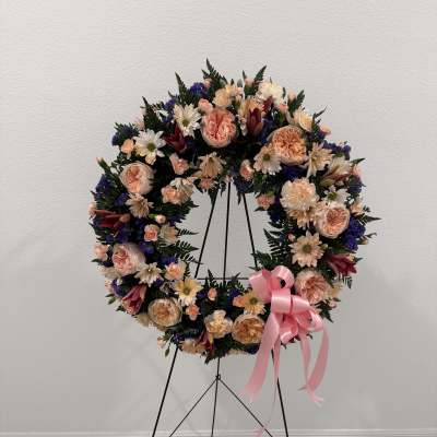 Large floral wreath on a black stand with a pink ribbon bow