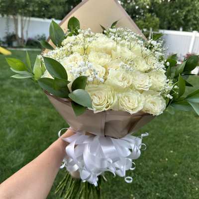 Bouquet of cream roses with baby's breath and greenery, wrapped in tan paper with a white ribbon