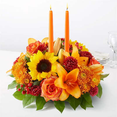 Orange and yellow floral centerpiece with two orange taper candles