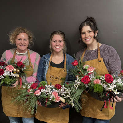 Three women holding holiday floral arrangements in shallow black containers