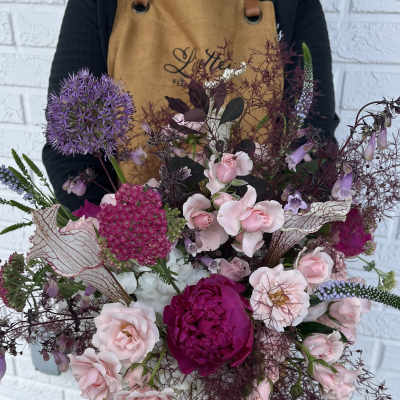 Large bouquet of pink and purple flowers held by a person in an apron