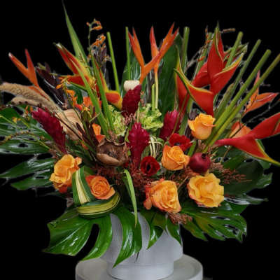 Tropical floral arrangement with orange roses and red heliconia in a white vase